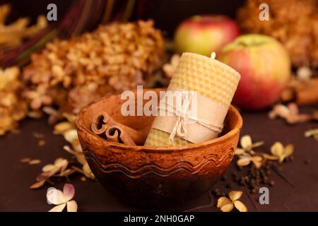 Bienenwachskerze von Hand, Zimt, Äpfel und trockene Hortensienblüten auf braunem Hintergrund. Honigaroma für Interieur und Tradition. Mockup, vorne Vie Stockfoto