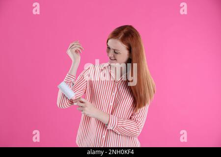 Junge Frau, die Kleidung putzt, mit Fusselrolle auf pinkfarbenem Hintergrund Stockfoto