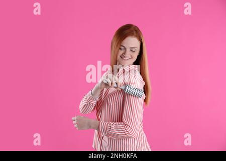 Junge Frau, die Kleidung putzt, mit Fusselrolle auf pinkfarbenem Hintergrund Stockfoto