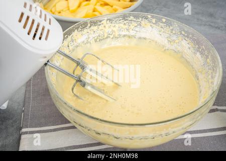 Kuchenteig mit einem elektrischen Mixer in einer Glasschüssel mischen. Apfelkuchen-Rezept Stockfoto