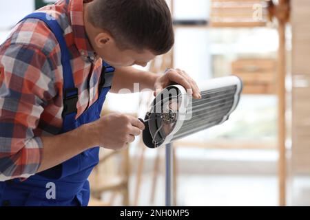 Professioneller Techniker, der elektrische Infrarotheizer mit Schraubendreher in Innenräumen repariert Stockfoto