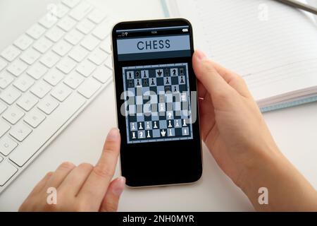Frau, die online Schach auf einem Smartphone spielt, am Tisch, Nahaufnahme Stockfoto