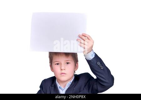 Ein Junge im Schulanzug mit einem Blatt A4-Papier während des Fernunterrichts, isoliert auf weißem Hintergrund Stockfoto