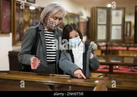 Zwischen einem Schulmädchen und einer älteren Tutorin in Gesichtsmasken während der Ausstellung in der Kunstgalerie Stockfoto