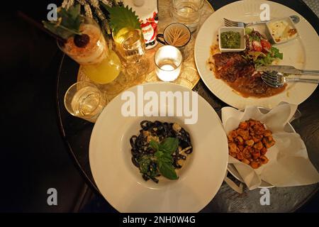 Nudeln mit schwarzer Tinte serviert mit knuspriger Hähnchenhaut und Rindfleisch-Steak Stockfoto