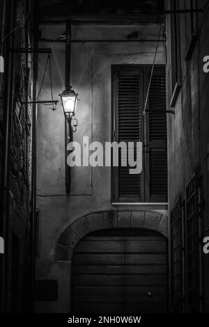 Dunkel-launisches, langbelichtetes Schwarz-Weiß-Straßenfoto einer alten Lampe, Toskana, Italien. Stern-Lichteffekt. Stockfoto