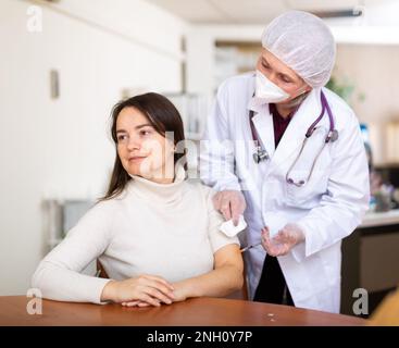 Fokussierte ältere Ärztin, die junge Frau impft Stockfoto