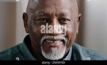 Männlicher Kopfschuss zu Hause ruhig ältere ältere Erwachsene Afrikaner 60s Mann freundliches Gesicht sitzt drinnen und schaut in die Kamera. Alter pensionierter birassistischer Geschäftsmann, der posiert Stockfoto