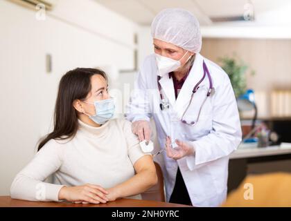 Fokussierte ältere Ärztin, die junge Frau impft Stockfoto