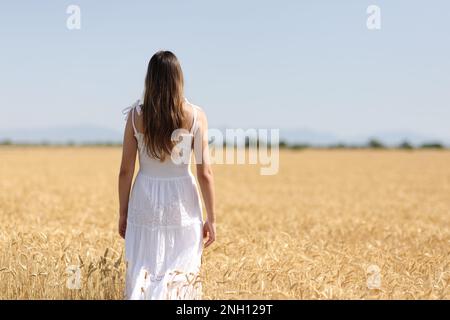 Rückansicht einer Frau in weißem Kleid, die auf einem Feld läuft Stockfoto