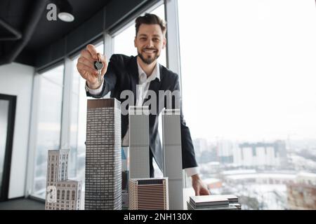 Konzentrieren Sie sich auf die Schlüssel in der Hand des Immobilienmanagers Hauseigentümer Geschäftsmann Bankverkäufer Kaukasier erfolgreicher Mann verkauft Immobilien aus einem neuen Apartment in der Nähe von 3D Stadtmodell im Büro mit Panoramafenster Stockfoto