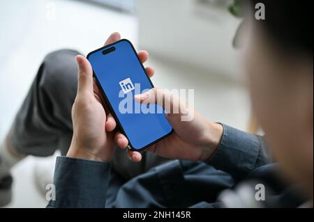 Chiang Mai, Thailand - Februar 17 2023: Nahaufnahme eines Asiaten, der LinkedIn auf seinem Smartphone verwendet. IPhone mit LinkedIn-Logo auf dem Bildschirm. Job und Inte Stockfoto