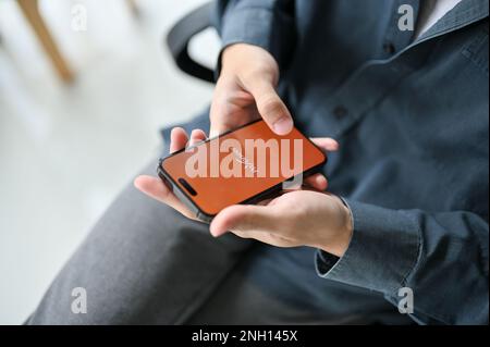 Chiang Mai, Thailand - Februar 17 2023: Draufsicht eines Mannes in Freizeitkleidung, der die mobile Payoneer-Anwendung an seinem Schreibtisch verwendet. IPhone mit Payoneer Logo auf sc Stockfoto