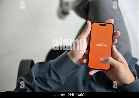 Chiang Mai, Thailand - Februar 17 2023: Draufsicht eines Mannes, der die mobile Payoneer-Anwendung an seinem Schreibtisch verwendet. IPhone mit Payoneer Logo auf dem Bildschirm. Internationa Stockfoto