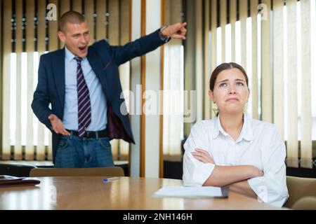 Emotionaler junger Chef beschimpft seine Sekretärin im Konferenzraum Stockfoto