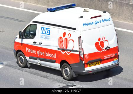 Bitte geben Sie Blood NHS-Werbespot und herzförmige Grafiken auf der Rückseite der Luftaufnahme des rot-weißen Ford Transit-Kleinbusses, der auf der britischen Autobahn fährt Stockfoto