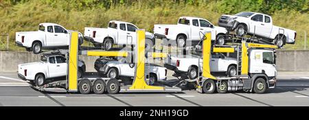 Sieben weiße Pickup-Lkw von Isuzu, die auf einen flexiblen, einstellbaren Pkw-Transporter verladen werden, der von einem lastkraftwagen gezogen wird, der auf der britischen Autobahn fährt Stockfoto