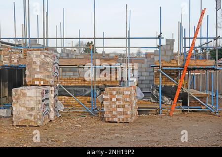 Baumaterialien gestapelt auf der Zugangleiter auf der Baustelle des Hauses in Position freistehende Hohlwände des Hauses aus Ziegelsteinen und Isolierblöcken UK Stockfoto