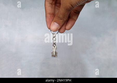 Handgehaltener Schlüsselanhänger in Hausform und Schlüssel mit Kopierbereich. Hausbesitzkonzept. Stockfoto