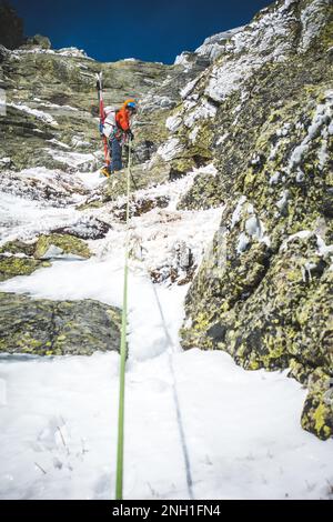 Der Mann mischte Eiskletterer mit Skiern auf dem Rücken, die auf Felsen lagen Stockfoto