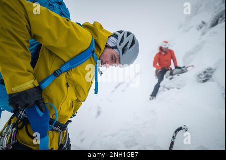 Ein Eiskletterer, der sich in verschneiter Landschaft auf die Beine stellt Stockfoto