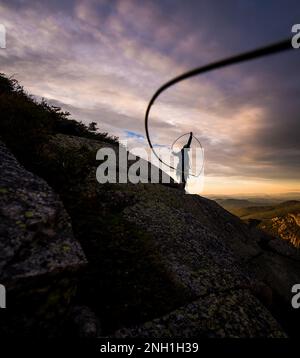 Eine Frau, die beim Sonnenuntergang über den Klippen ein Seil hochklettert Stockfoto