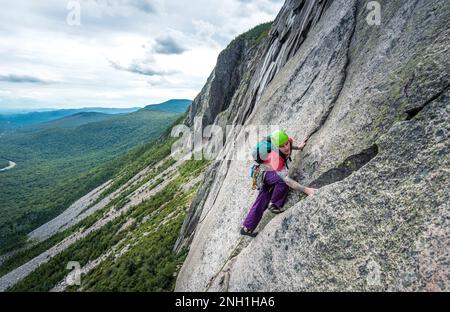 Ein Mann klettert steile Risse auf einer Klippe mit einem Tal dahinter Stockfoto
