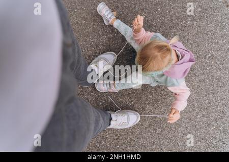 Ein stilvolles Mädchen im Hoodie-Hooligan löst Dads Schnürsenkel Stockfoto