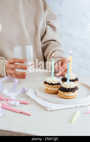Mit Kerzen geboren, hält ein Mädchen ein Glas mit einem Drink im Rücken Stockfoto