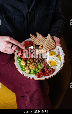 Ein Mann isst ein englisches Frühstück mit Rührei, Speck, Bohnen Stockfoto