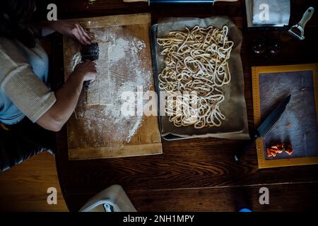 Blick von oben auf eine Frau, die hausgemachte Pasta auf dem Küchentisch schneidet Stockfoto