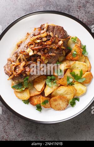 Traditionelles, trocken gereiftes Roastbeef mit gebratenen Zwiebelringen und Kartoffelschnitzel auf dem Teller auf dem Tisch. Vertikale Draufsicht von oben Stockfoto