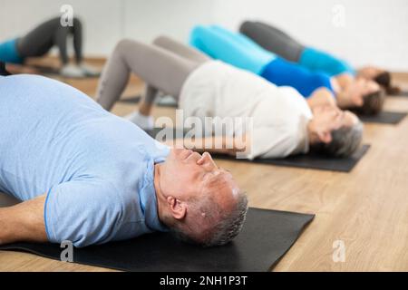 Gruppe junger, reifer alter Menschen in Sportbekleidung, die Pilates während des Liegens auf Matten im Rehabilitationszentrum treiben Stockfoto