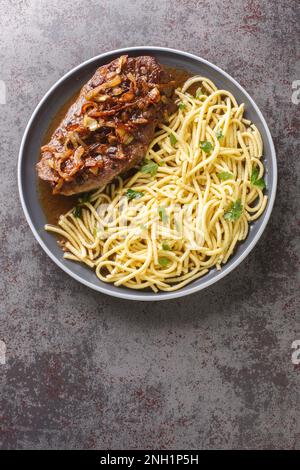 Traditionelles, trockenes, gereiftes Roastbeef mit gebratenen Zwiebelringen und schwäbischem Spaetzle auf dem Teller auf dem Tisch. Vertikale Draufsicht von oben Stockfoto