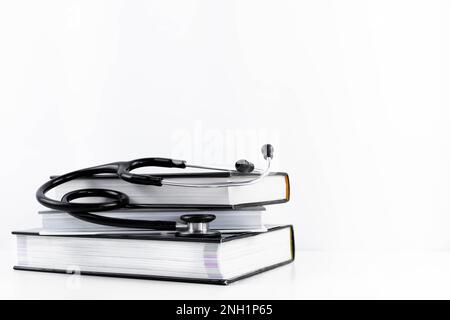 Stethoskop, das sich mehrere Medizinbücher anhört. Weißer Hintergrund mit Kopierbereich. Isoliertes Lernkonzept Medizin, Kardiologie, Gesundheit Stockfoto