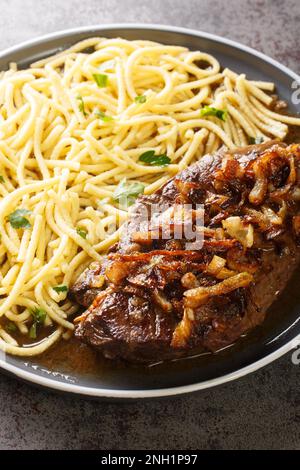 Traditionelles, trockenes, gereiftes Roastbeef mit gebratenen Zwiebelringen und schwäbischem Spaetzle auf dem Teller auf dem Tisch. Vertikal Stockfoto