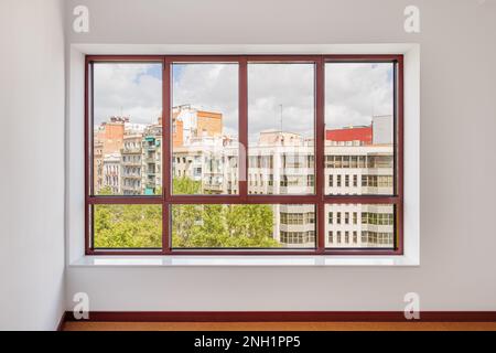 Großes Fenster im Zimmer mit breiter Fensterbank. Fenster in braunem Kunststoffrahmen. Durch das Fenster können Sie beobachten, was auf der Straße passiert und Stockfoto