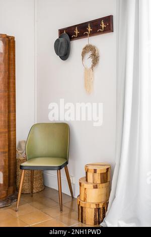 Eingangshalle mit weißem Heu im stimmungsvollen Bo-Ho-Stil. An der Wand befindet sich ein geschnitzter Kleiderbügel für Oberbekleidung und ein schwarzer Hut für Männer. Schönes grünes Holz Stockfoto