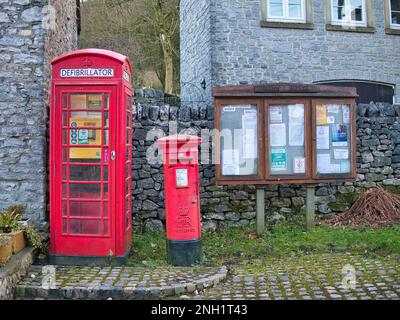 Ein Notfall-Defibrillator in einer alten roten Telefonzelle im Dorf Taddington in Derbyshire, Großbritannien. Ein rotes Postfach und eine Gemeindeanklagemappe werden angezeigt o Stockfoto