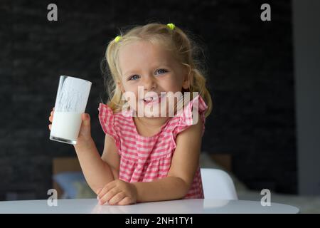 Porträt eines kleinen blonden Mädchens, das ein Glas laktosefreien Joghurt am Tisch trinkt und lächelt, Vorschulkind genießt Bio-Getränk, bekommt Kalzium Stockfoto