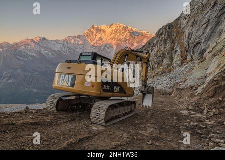 Arbeiten Sie in großen Höhen in den Bergen. Caterpillar-Hydraulikbagger baut eine unbefestigte Straße. Kat Stockfoto