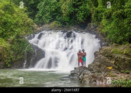 Zwei junge einheimische Embera-Männer in traditioneller Kleidung stehen an einem Wasserfall am Fluss Chagres in Panama. Stockfoto