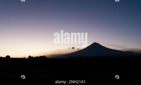 Ein beeindruckender Sonnenuntergang über einem Berg mit dramatischen Silhouetten im Hintergrund Stockfoto