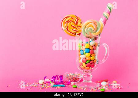 Bunte Süßigkeiten im Becher auf dem Tisch auf hellem Hintergrund. Große, geschwungene Lutscher. Kreatives Konzept eines Glases voller köstlicher Süßigkeiten aus dem Stockfoto