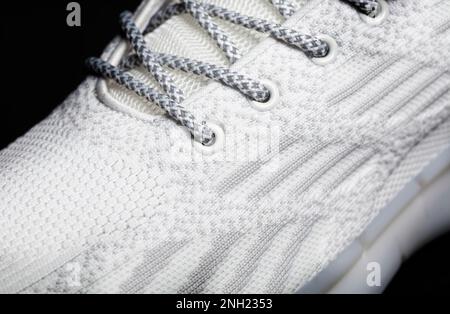 Teil eines Sneakers aus weißem Stoff mit Schnürsenkeln auf dunklem Hintergrund. Stockfoto