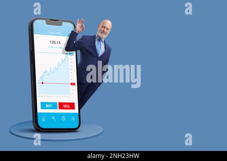 Erfolgreicher Geschäftsmann, der das OK-Zeichen macht und im Online-Handel Geld verdient: Finanzanwendung auf großem Smartphone, leerer Kopierbereich Stockfoto