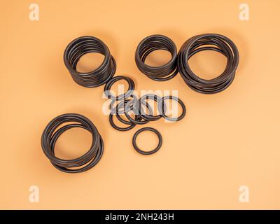 Hydraulische und pneumatische O-Ringe in Schwarz in verschiedenen Größen auf orangefarbenem Hintergrund. Gummidichtungen für Rohrleitungen. Speicherplatz kopieren. Stockfoto