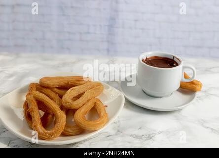 Teller mit Churros mit Zucker und einer Tasse heißer Schokolade auf Marmorhintergrund, typisches spanisches Frühstück Stockfoto