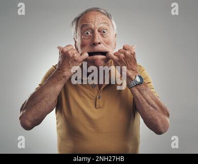 Immer jung im Herzen. Studiofoto eines älteren Mannes, der ein lustiges Gesicht vor grauem Hintergrund macht. Stockfoto