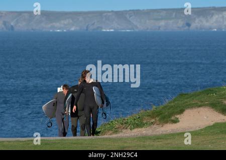 Drei Surfer, die ihre Surfbretter tragen und den Küstenpfad bei Newequay in Cornwall in England in Großbritannien entlang wandern. Stockfoto